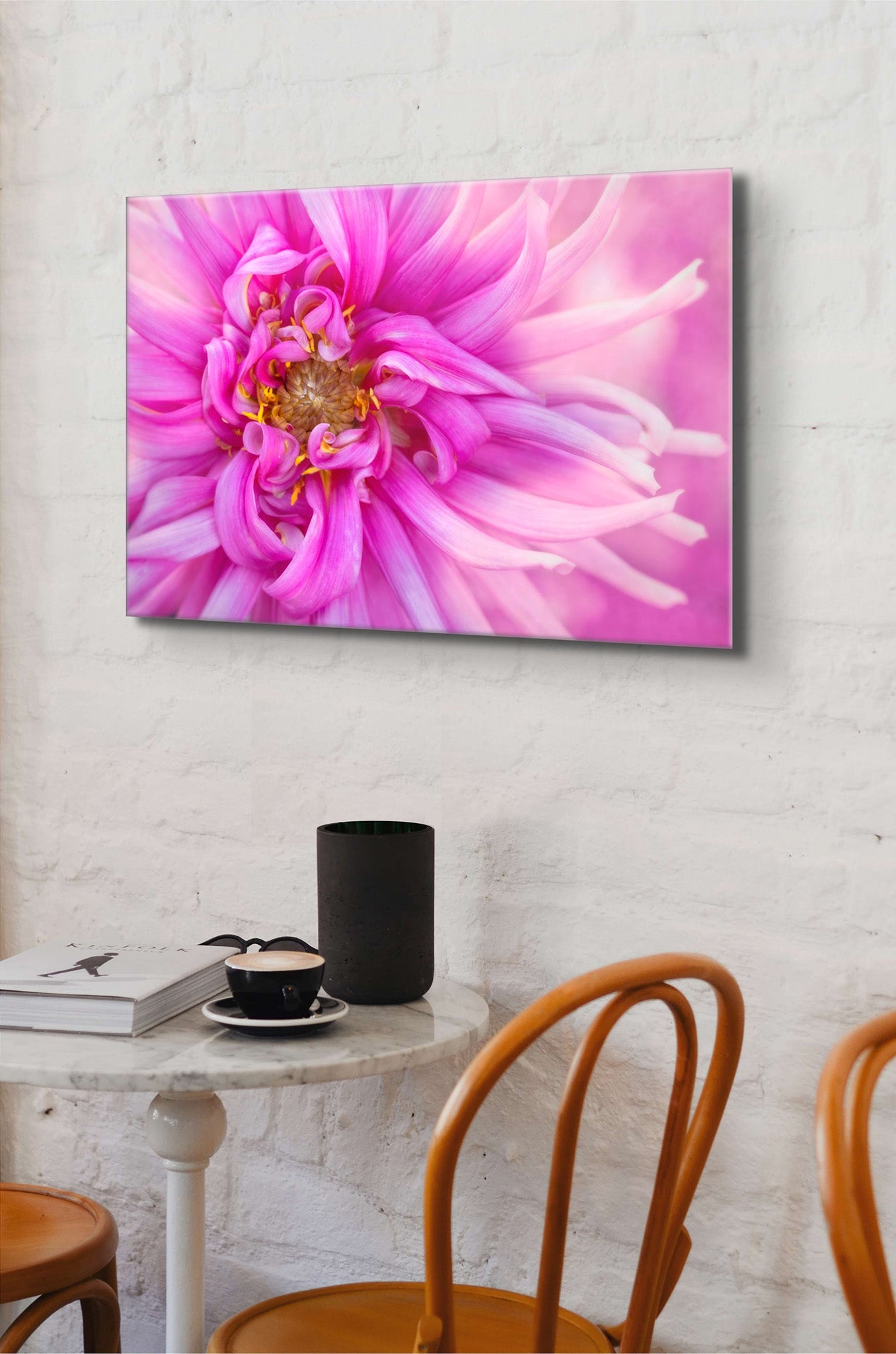 Photograph hanging on the wall of a coffee shop. Hanging over a table and chairs. The photograph is a vibrant macro photo of a pink dahlia by Cameron Dreaux. Printed on high-quality metal. 