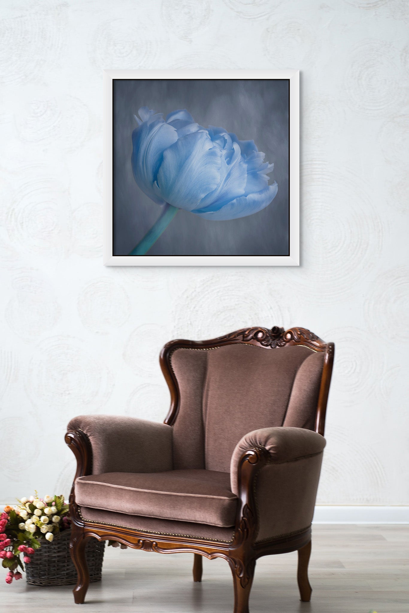 Picture hanging on the wall of a room. The room has a chair in the middle of the room. The picture is a fine art photograph of a blue tulip by Cameron Dreaux. 