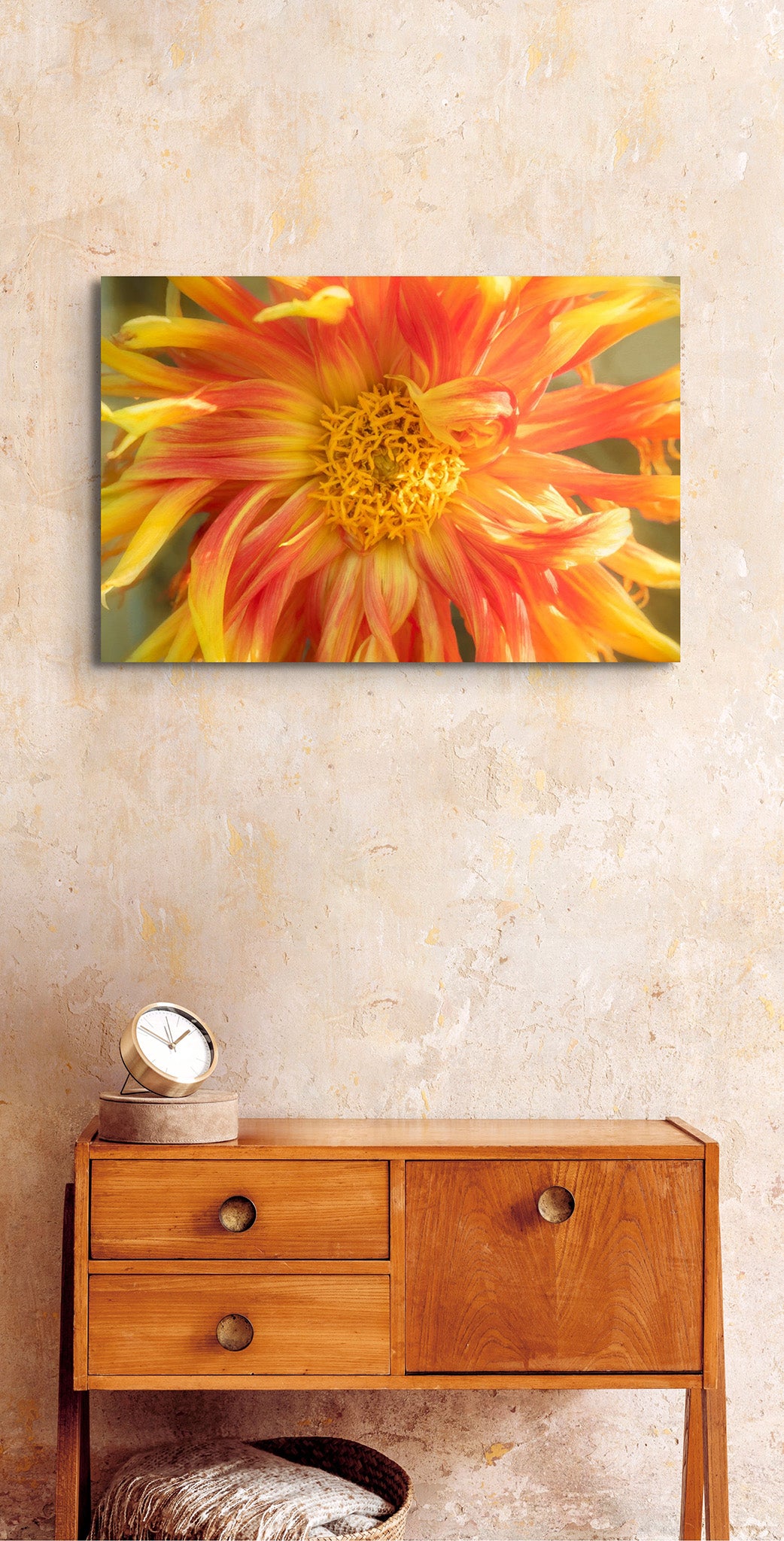 Picture hanging on wall of a room with a table next to a wall. The picture is a photograph of a flowing yellow dahlia flower by Cameron Dreaux. 