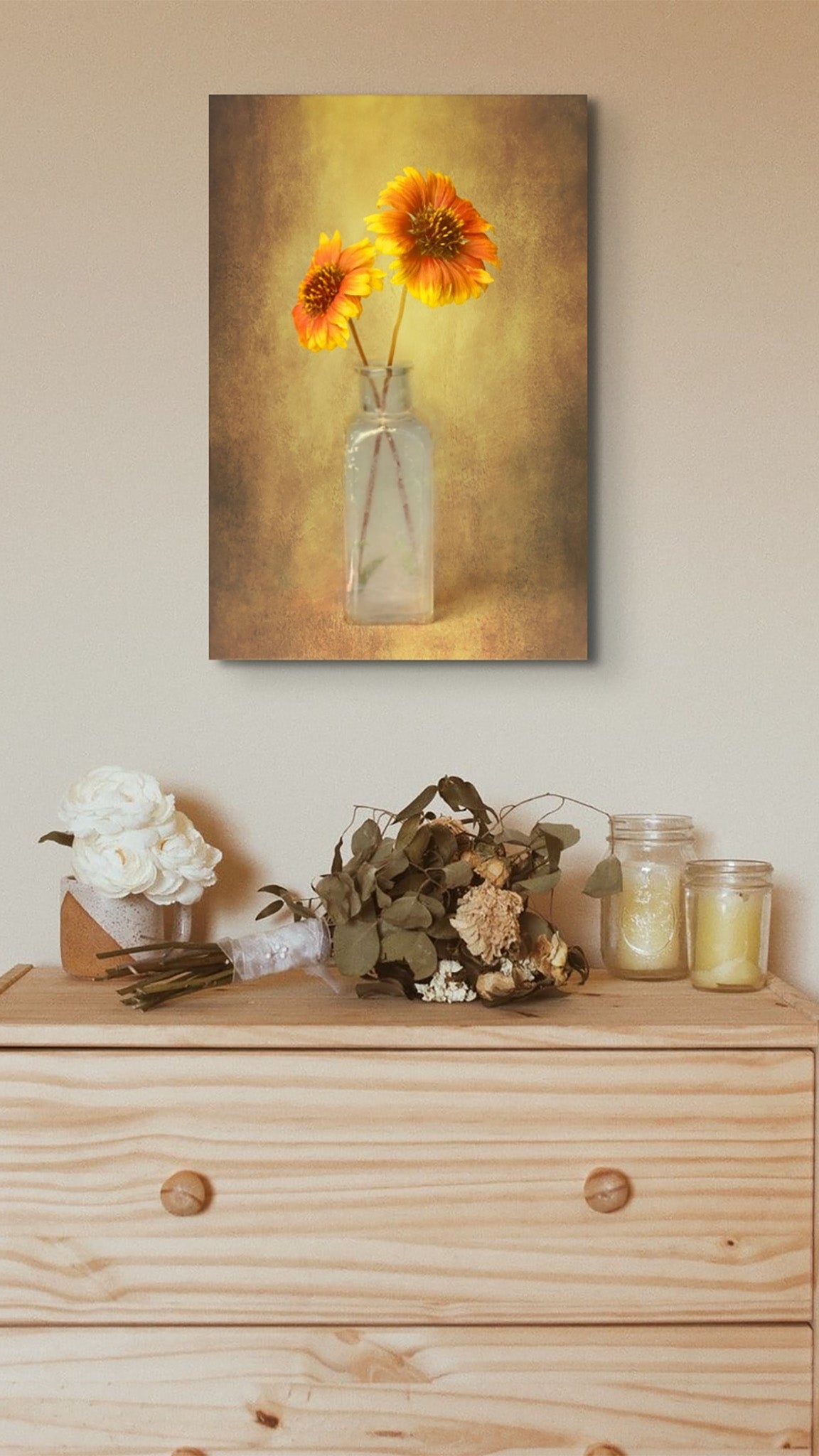 Picture hanging on the wall of a room over a chest of drawers. The picture is a fine art photograph of yellow treasure flowers in old bottle titled "Yellow Treasure" by Cameron Dreaux of Dreaux Fine Art.