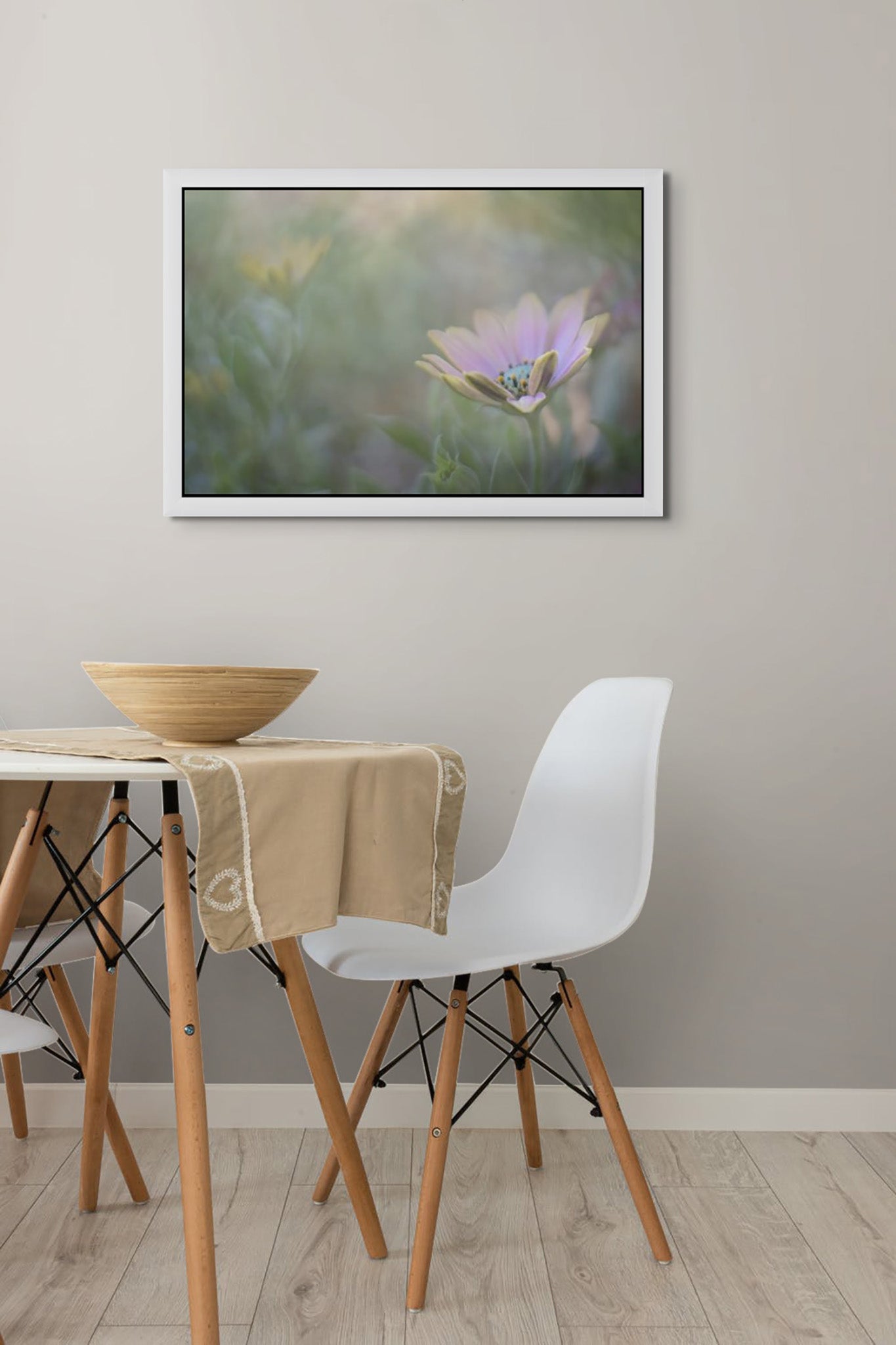 Photo mounted on the wall of a room. The photo is framed with White Wedge Float Frame. There is a kitchen table and chairs in the room. The Photograph is by Cameron Dreaux of Dreaux Fine art. The photo is a purple coastal flower on a backdrop of green. Sun is shining some light through at the top of the photograph,