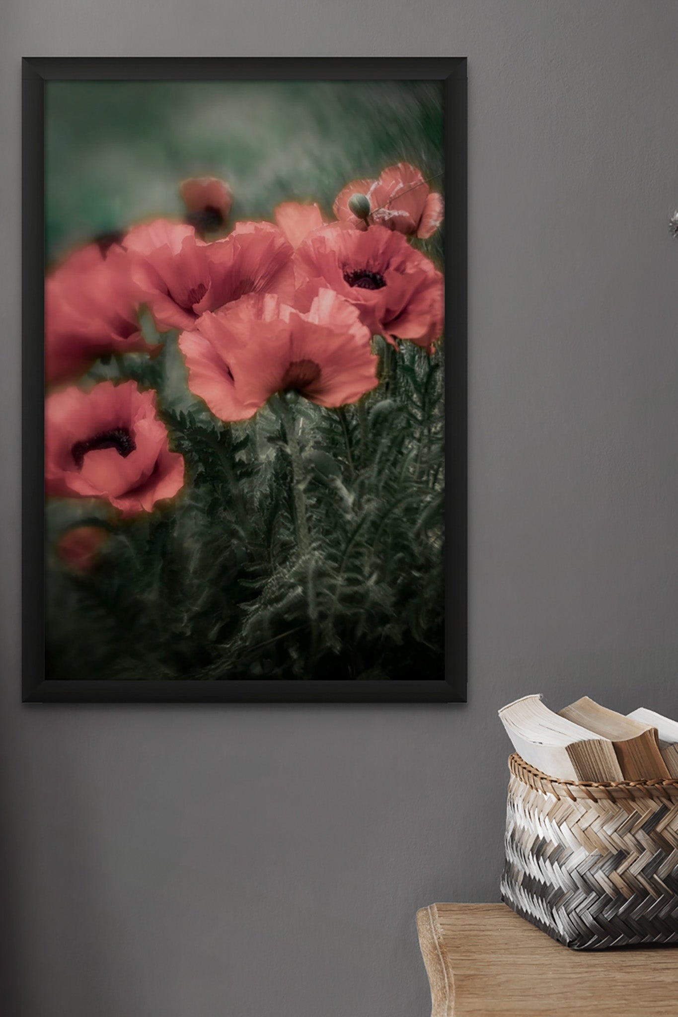 Picture in a floating frame hanging on the wall of room. There is a table in the rooms and books on the table. The picture is a fine art photograph of red poppies on dark green stormy background by Cameron Dreaux. 