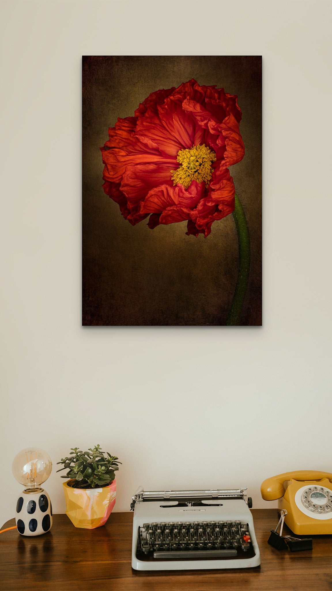 Picture hanging on the wall of a room. There is a desk with a typewriter. The picture is a fine art flower photography titled "Confidence" by Dreaux Fine Art. 