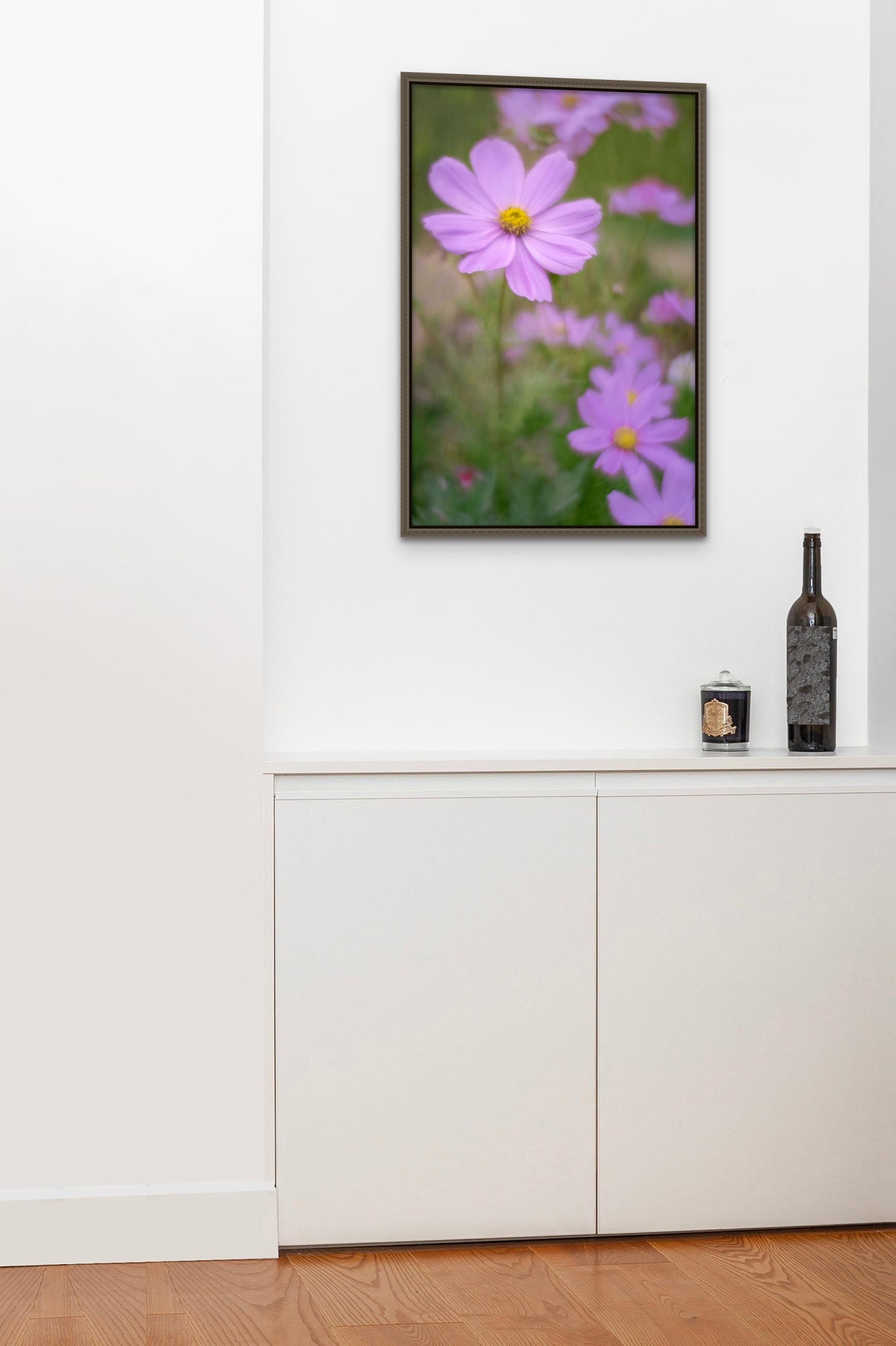 Float frame picture hanging on the wall of a mini bar area. There is a glass and a bottle of wine sitting on the bar. . The picture is a fine art flower photograph of a purple Cosmopolitan flower by Cameron Dreaux. 