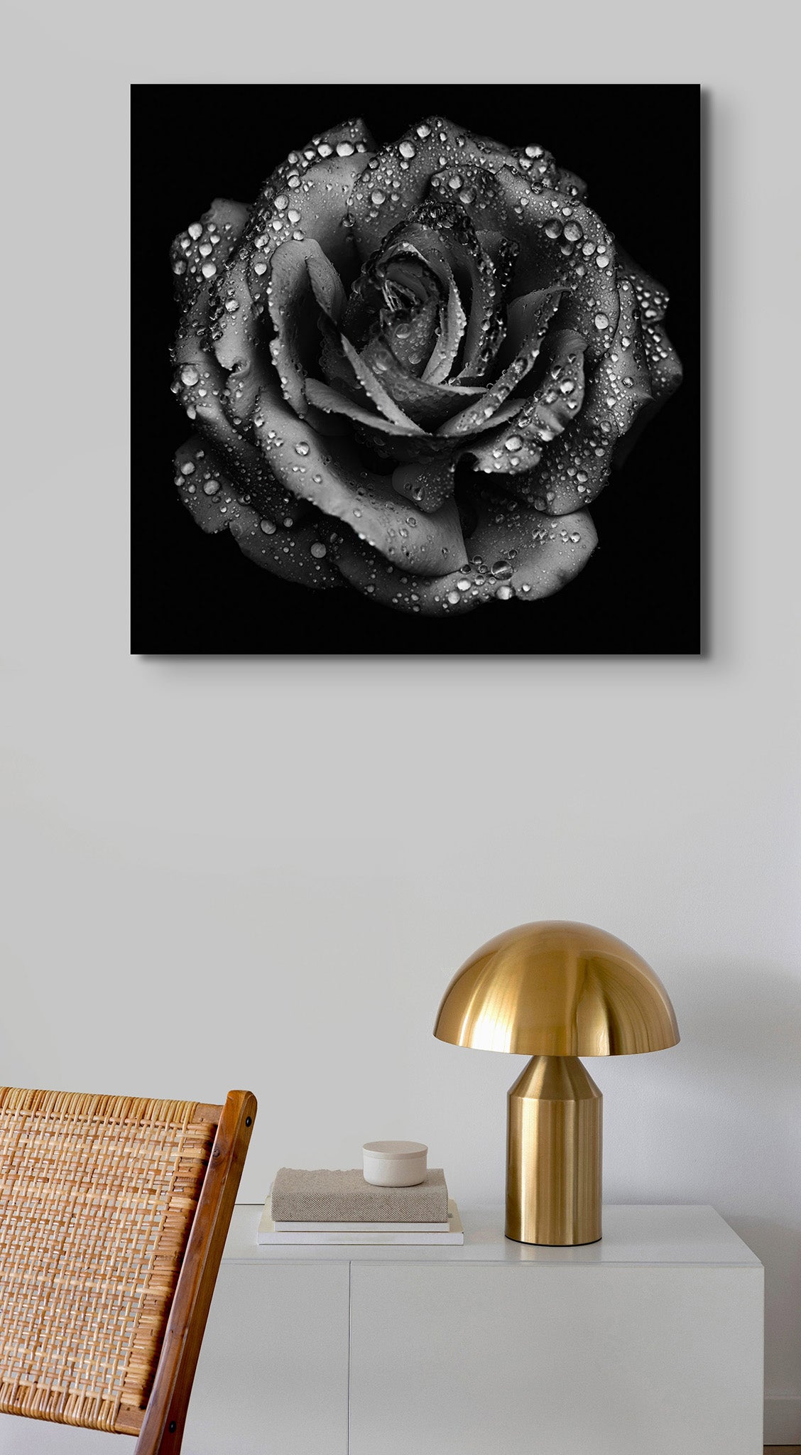 Picture hanging on the wall of the room. There is a gold lamp and a chair in the frame. The picture is a black and white fine art photograph of a rose by Cameron Dreaux. 