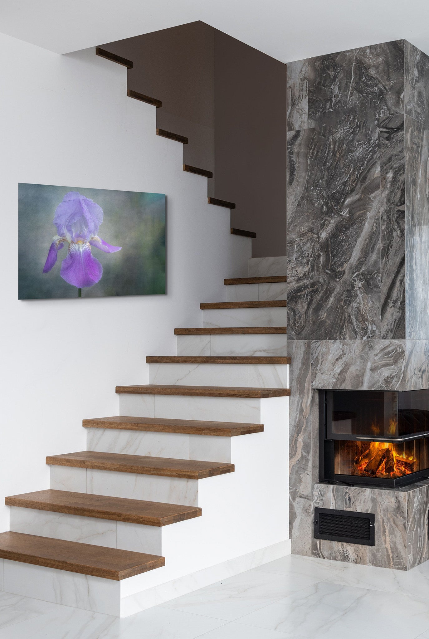 Picture hanging on the wall of a living room. There is a fireplace with a fire going and a staircase. The picture is on the wall by the staircase. The picture is a fine art flower photograph of a purple Iris flower titled "Empowered" by Cameron Dreaux of Dreaux Fine Art.