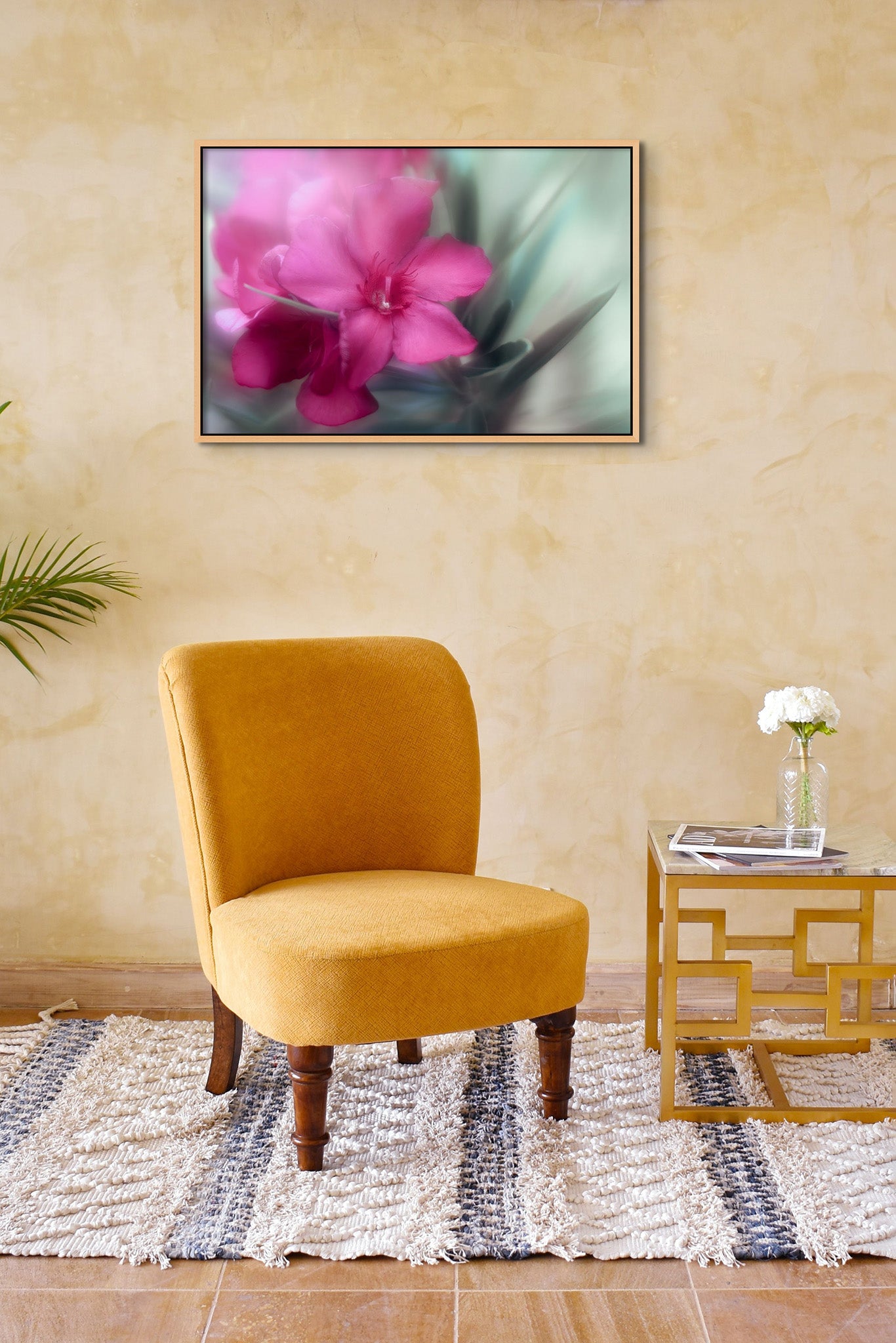 Photography of a red oleander by Cameron Dreaux, printed on metal. Photograph is hanging on the wall of a yellow room. Room has a yellow chair and end table. 
