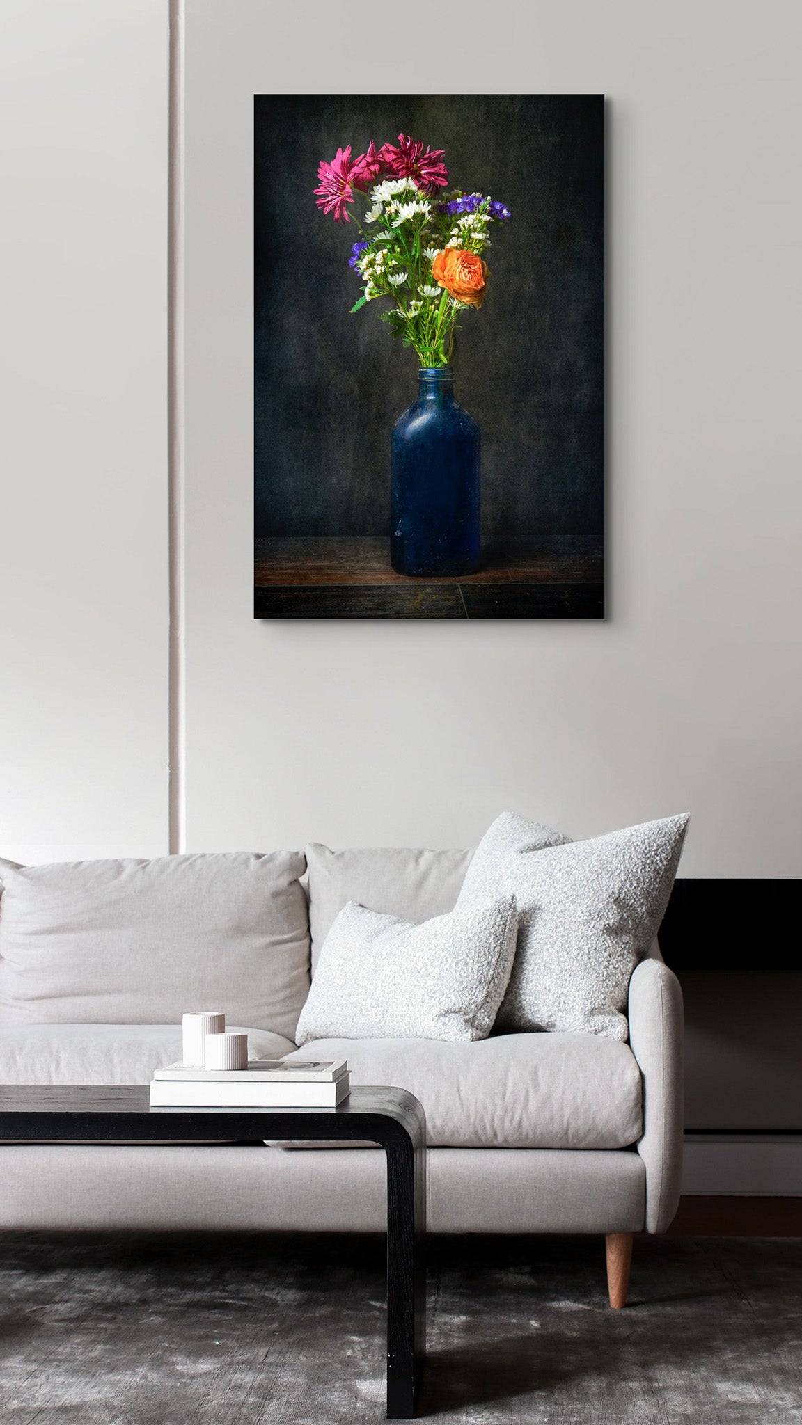Picture hanging on the wall of a living room. The picture is a fine art flower photograph of a bouquet of flowers in an old bottle titled "Tangy Resolve" by Cameron Dreaux of Dreaux Fine Art.