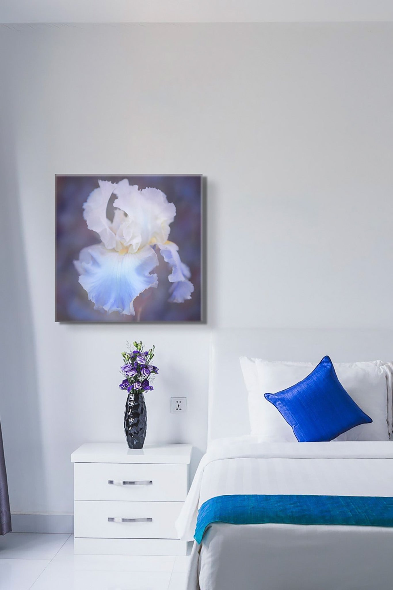 Picture hanging on the wall of the bedroom. The bed is made, and there is a blue pillow. The picture is a blue and white dahlia photograph by Cameron Dreaux. 