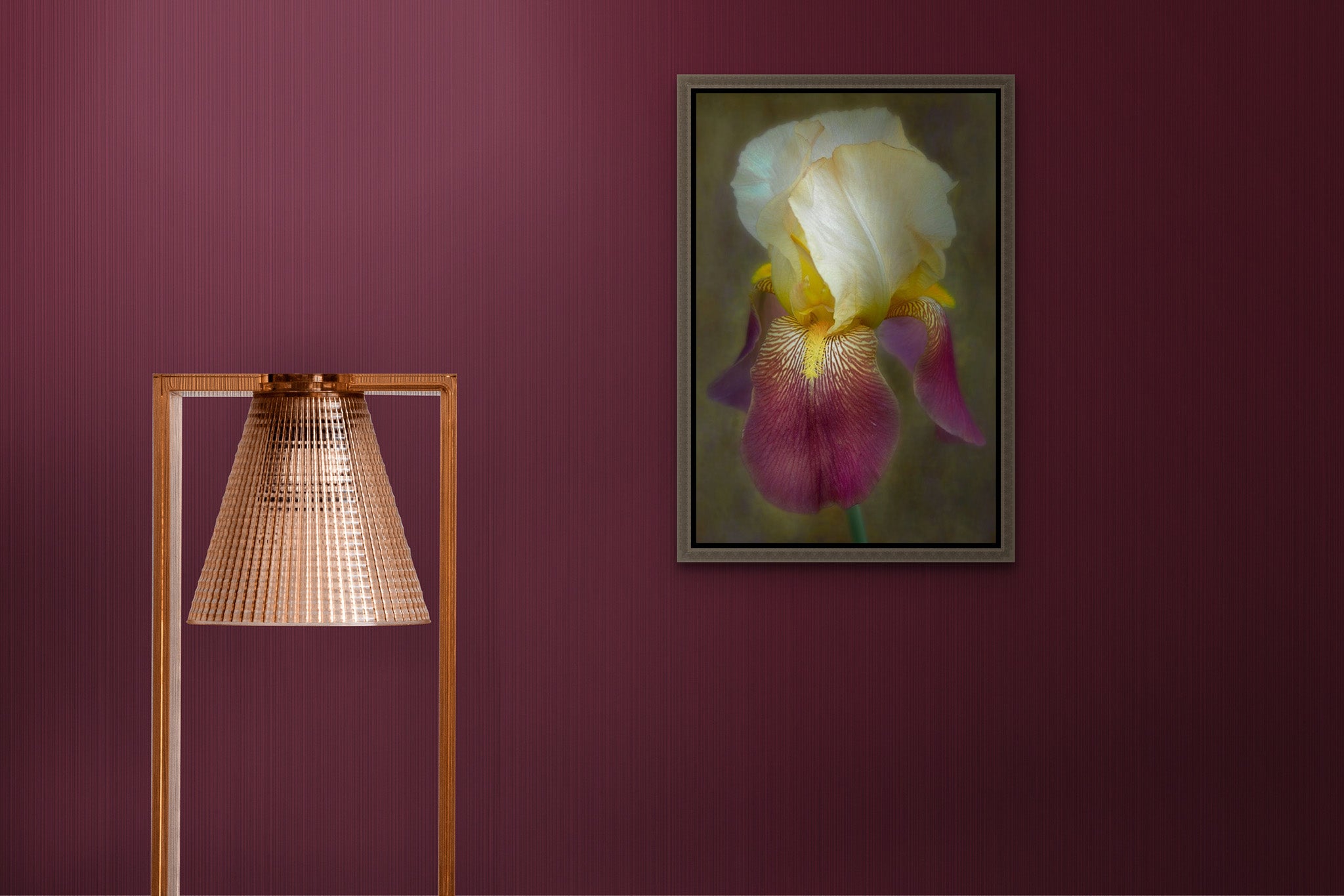 A picture is hanging on the wall of a room. The picture is a metal print and has a floating frame. There is a copper-colored lamp in the frame. The picture on the wall is a photograph of an Iris by Cameron Dreaux. 