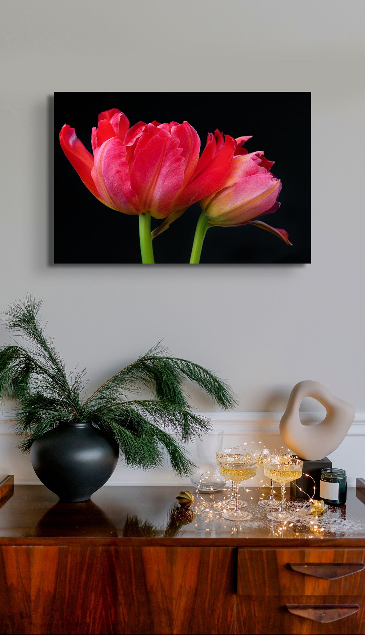 A picture on the wall of a room. The picture is a flower photograph called "Is it Dark Out" by Cameron Dreaux. Is it Dark Out is a picture of two magenta tulips on a black background. 