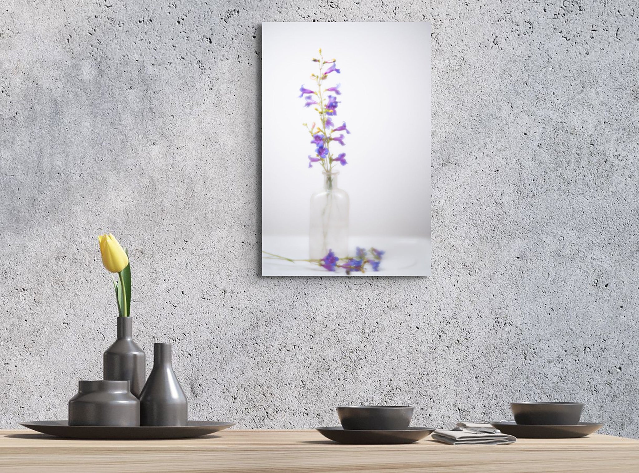Picture hanging on the wall of a dining room with a set table. The picture is a fine art photograph of wildflowers in a jar by Cameron Dreaux. 