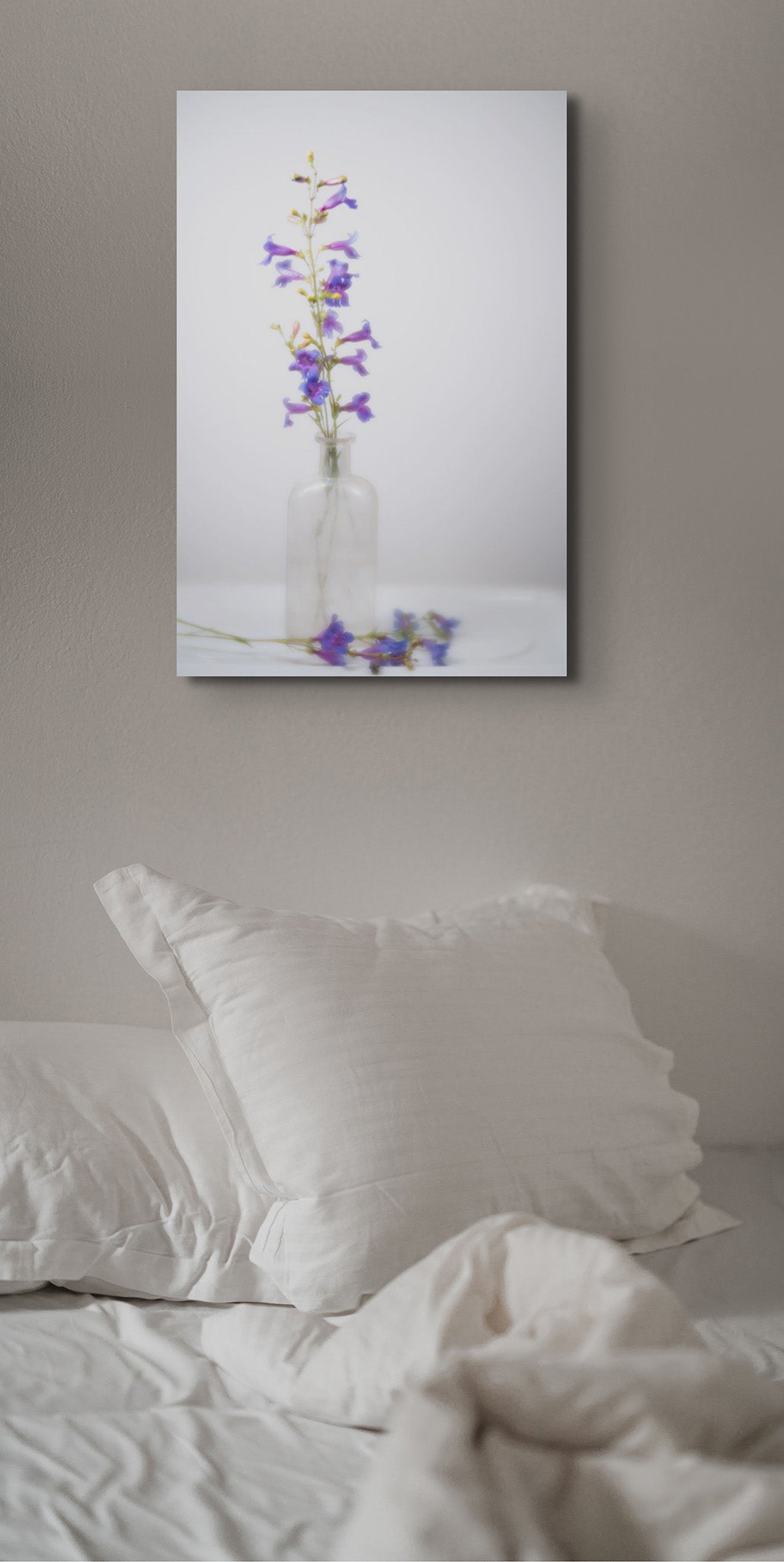 Picture hanging on the wall of a bedroom. The picture is a fine art photograph of wildflowers in a jar by Cameron Dreaux. 