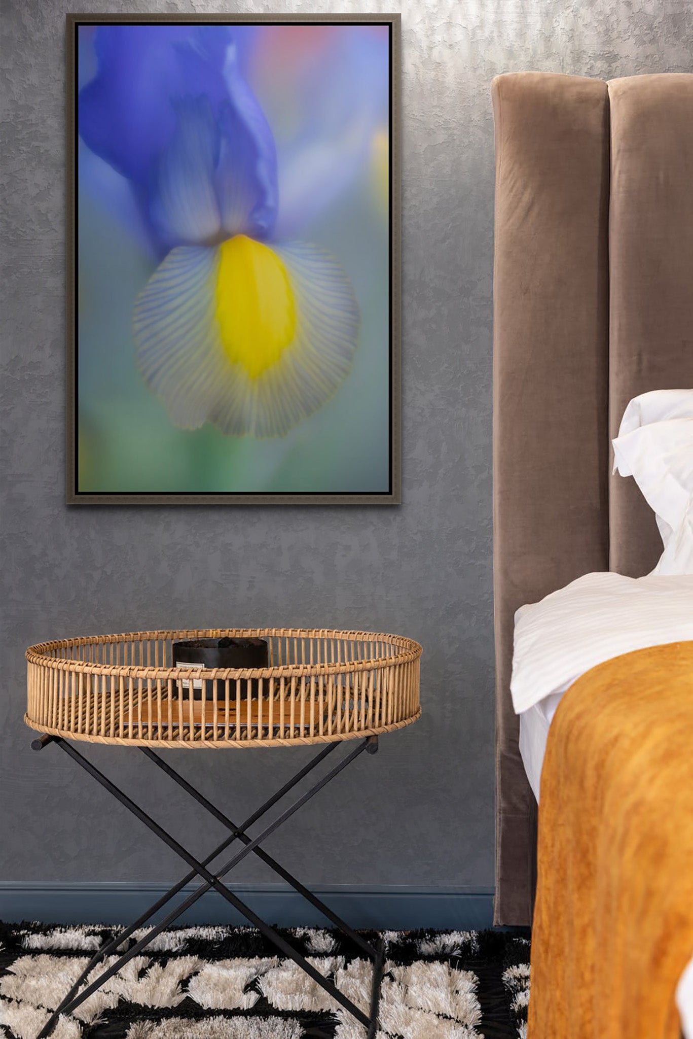 Picture hanging on the wall of a bedroom with a floating frame. There is a bed and a bassinet. . The picture on the wall is a fine art photograph of blue and yellow Iris by Cameron Dreaux. 