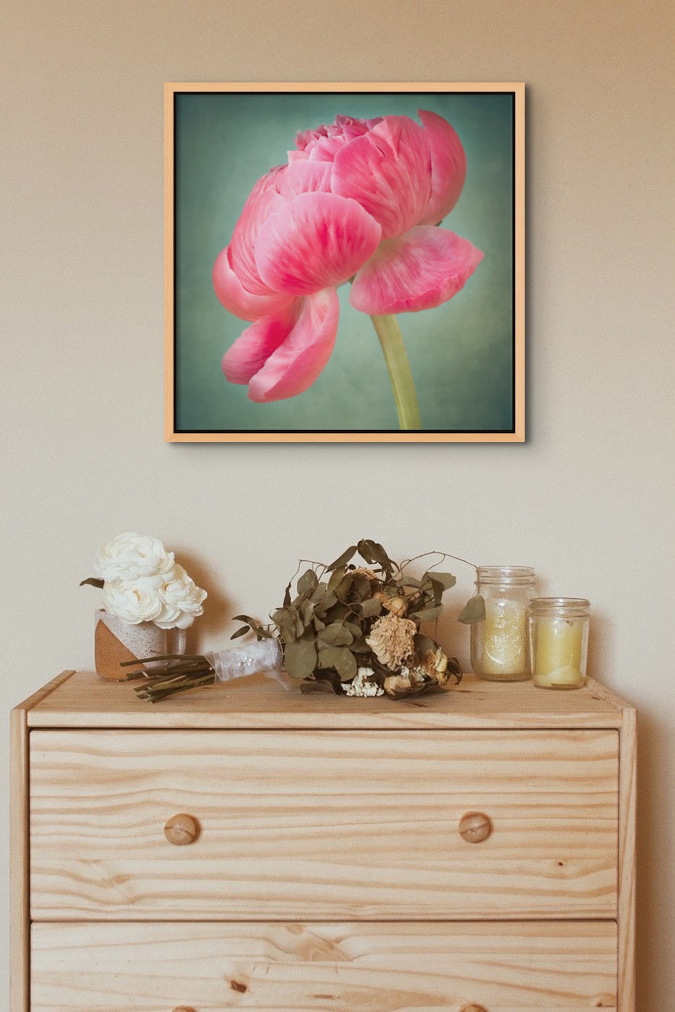 Picture hanging on a wall. Under the picture,  there is a chest of drawers. On top of the chest of drawers are various items.The picture is a metal print photograph of a pink peony flower on a greenish background by photographer Cameron Dreaux. 