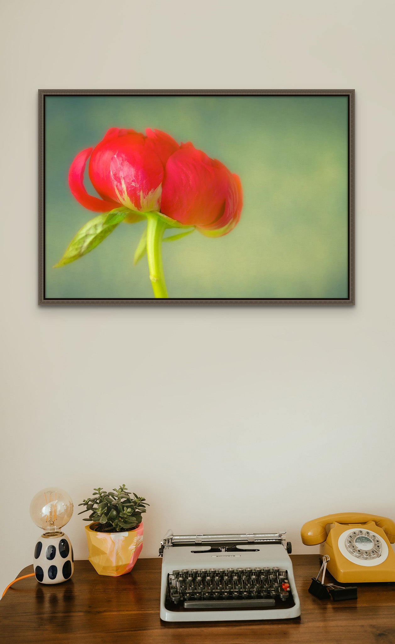 Picture hanging on a wall over a desk with a typewriter. The picture on the wall is a flower photograph of Red Peony on green background by Cameron Dreaux. 